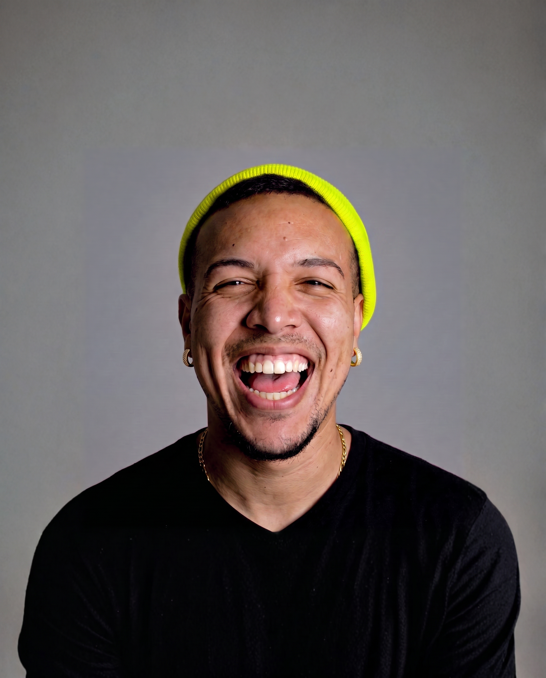 Retrato de Marlon Ribeiro sorrindo, de gorro amarelo neon, em estúdio